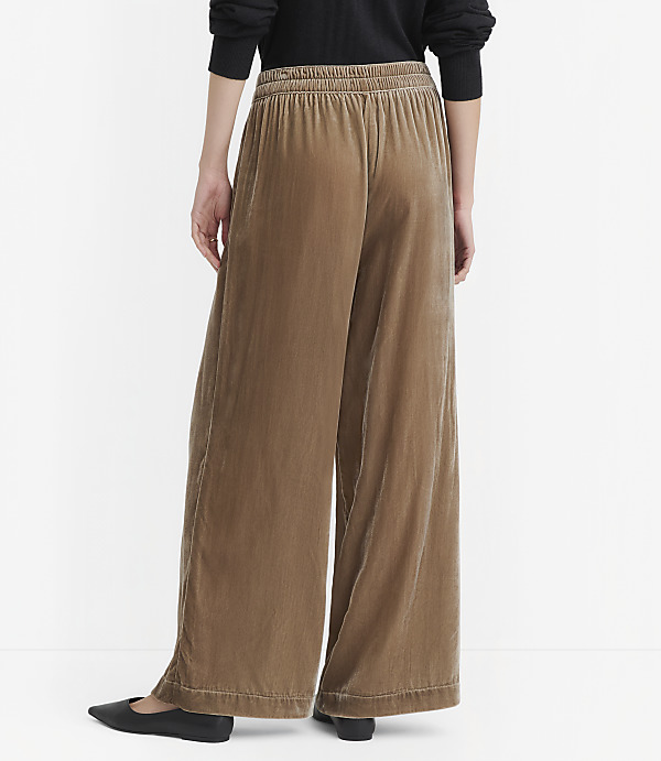 A person wearing wide-leg velvet pants stands against a plain white background.