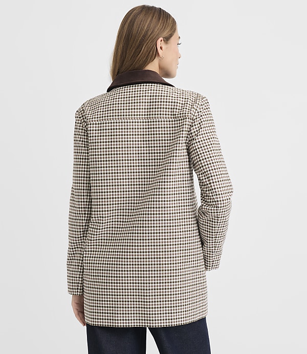 A woman in a checkered jacket stands against a plain gray background.