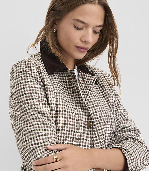A woman in a brown and white gingham jacket with a corduroy collar poses against a plain gray background.