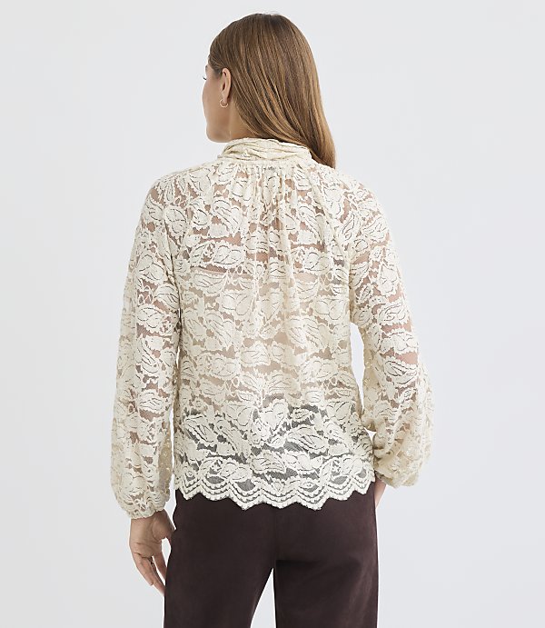 A woman in a cream lace blouse stands against a plain white background.