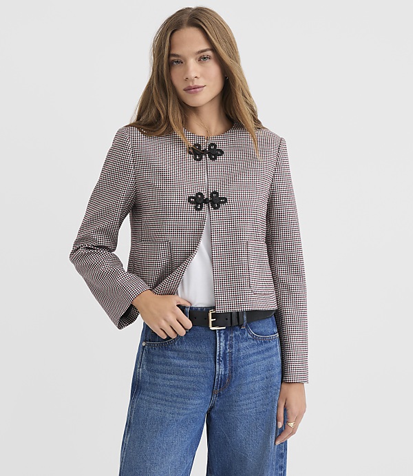 A woman in a patterned jacket and jeans stands against a plain white background.