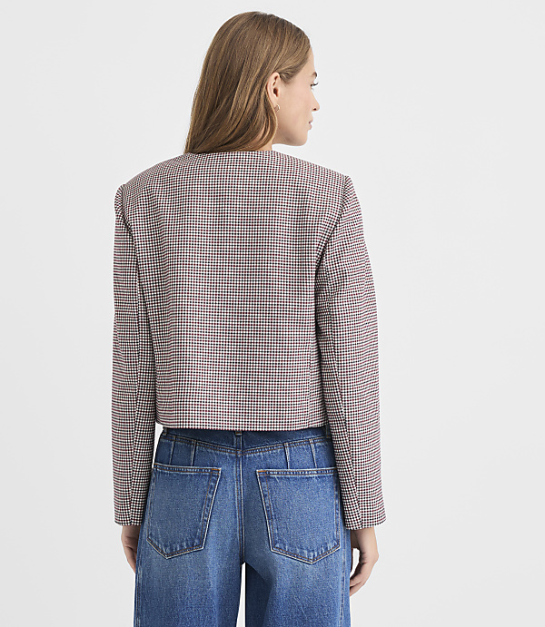 A woman in a patterned jacket and jeans stands against a plain white background.