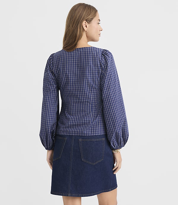 A woman in a blue plaid puff-sleeve top and denim skirt stands against a plain white background.