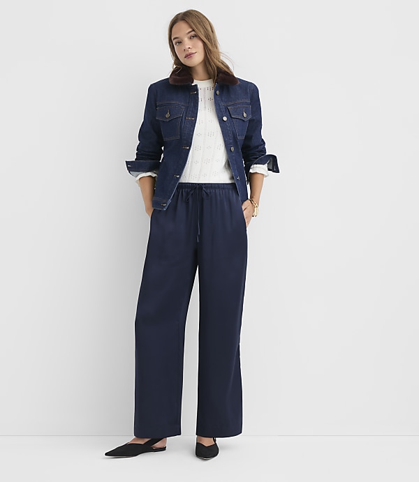 A woman in a denim jacket and wide-leg pants stands against a plain white background.
