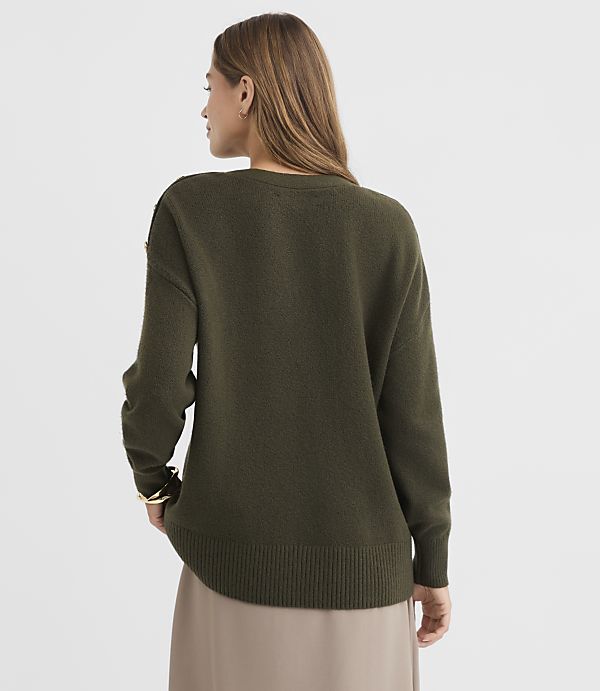 A woman in a green sweater stands against a plain, light gray background.