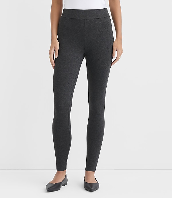 A person wearing dark gray leggings and black ballet flats stands against a plain white background.