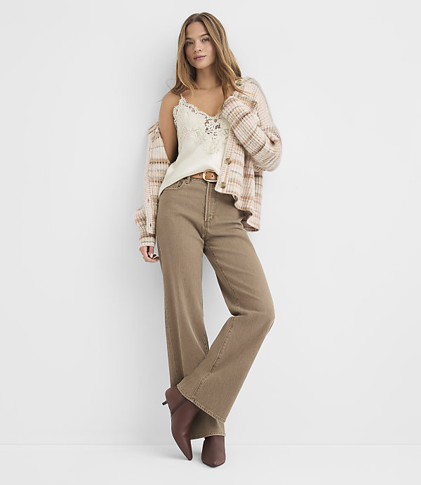 A young woman in a cream lace camisole, a plaid cardigan, and brown wide-leg jeans stands against a plain white background.