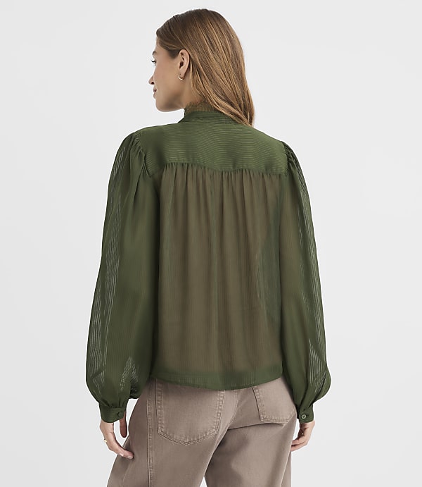 A woman in a green blouse stands against a plain white background.