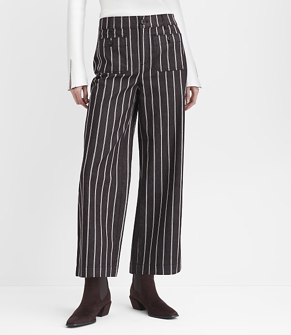 A person stands in front of a white background wearing brown and white striped wide-leg pants and dark brown boots.