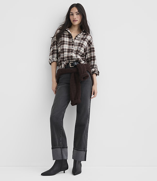A woman in a plaid shirt and cuffed jeans stands against a plain white background.