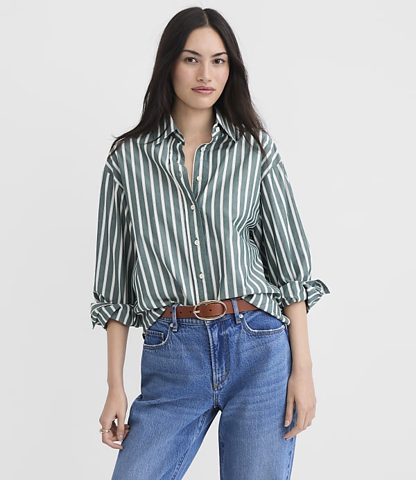 A woman in a green and white striped shirt and blue jeans stands against a plain white background.