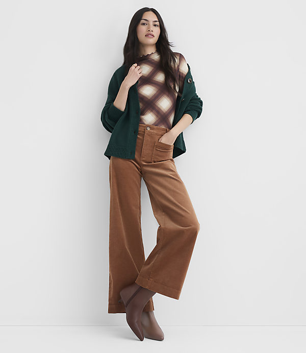 A woman in a patterned top, green cardigan, and brown corduroy pants stands against a plain white background.