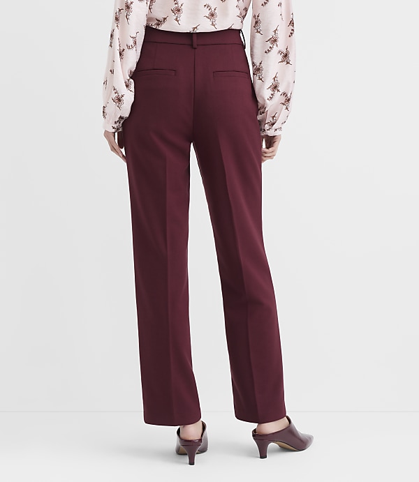 A person wearing burgundy pants and a floral blouse stands against a plain white background.