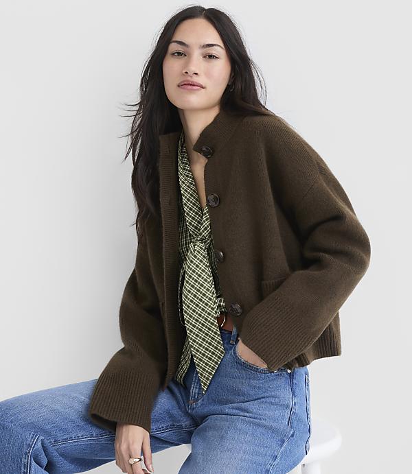 A woman in a brown cardigan and green patterned blouse poses against a plain white background.