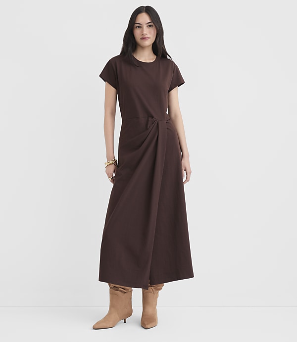 A woman in a brown dress and boots stands against a plain white background.