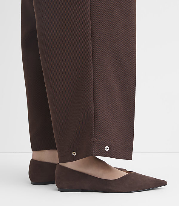 Brown suede flats peek out from beneath the hem of brown trousers adorned with silver buttons.