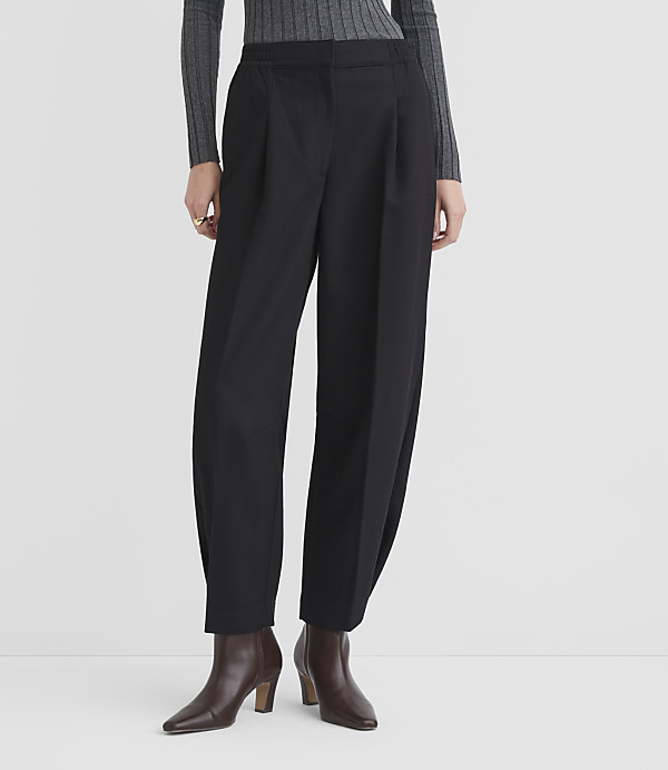 A person stands in black pleated trousers and brown ankle boots against a plain white background.