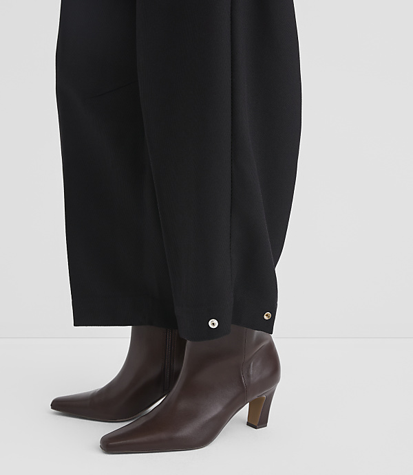 Black wide-leg trousers with silver button details are worn over brown leather ankle boots against a plain white background.