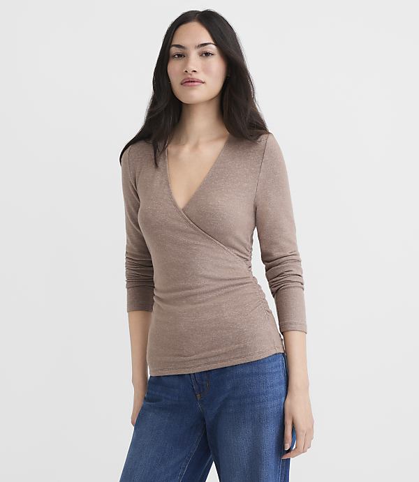 A woman in a brown wrap top and blue jeans stands against a plain white background.