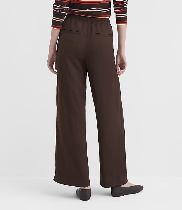A person wearing brown wide-leg pants and a striped sweater stands against a plain white background.
