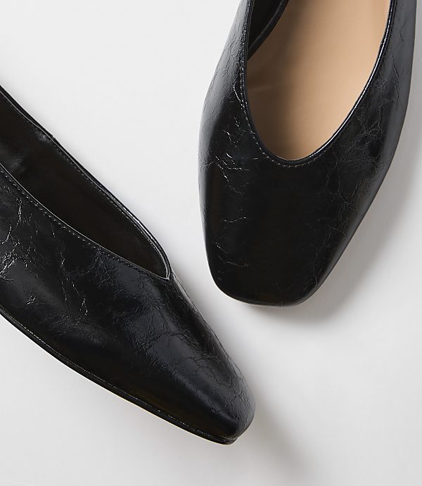 Two black, square-toed flats with a slightly crinkled texture are positioned on a plain white background.