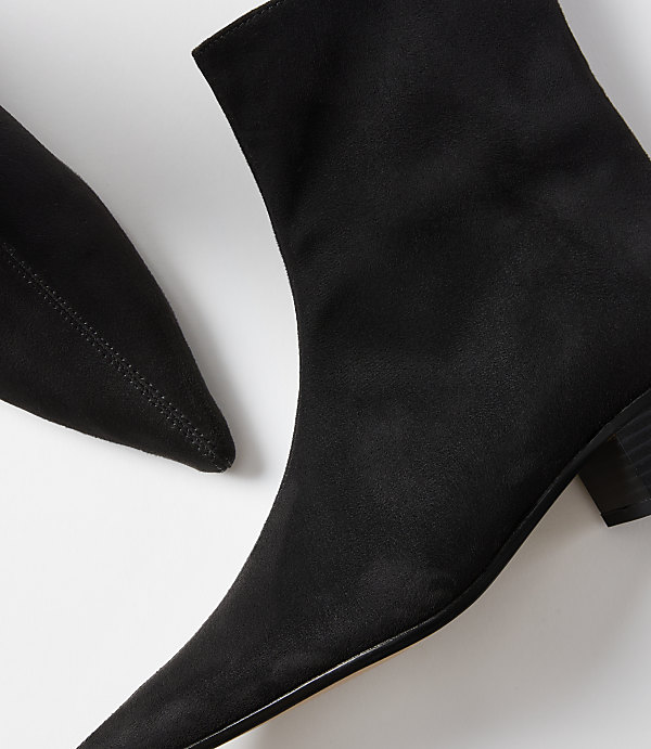 A close-up of two black pointed-toe ankle boots with a white background.