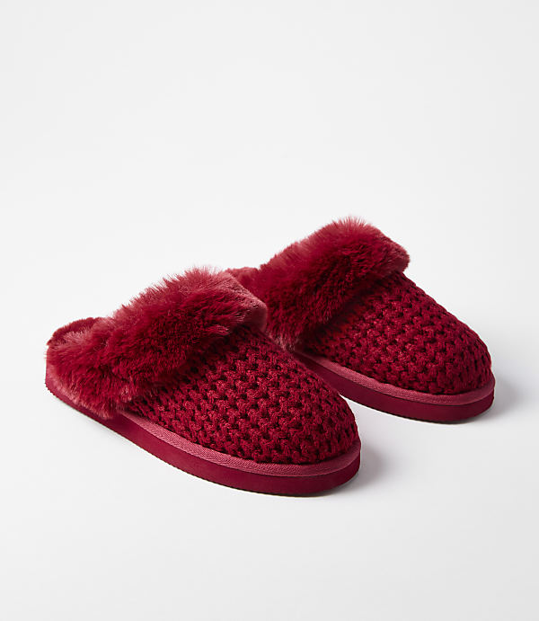 A pair of plush red knit slippers with faux fur trim rests on a plain white background.