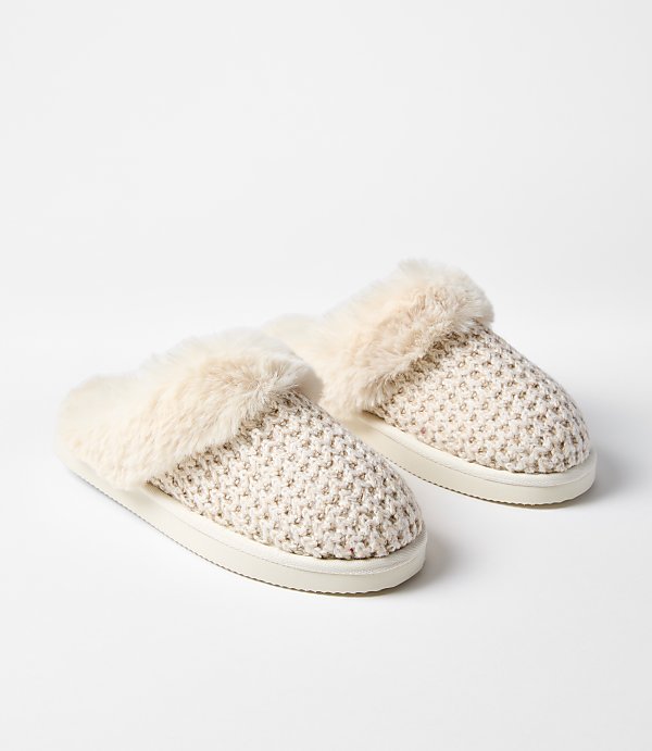 A pair of cream-colored, fuzzy slippers rests on a plain white background.