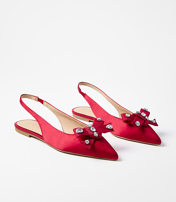 A pair of red satin slingback flats adorned with jeweled bows rests on a plain white background.