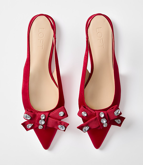 A pair of red satin slingback flats with jeweled bows are displayed against a plain white background.