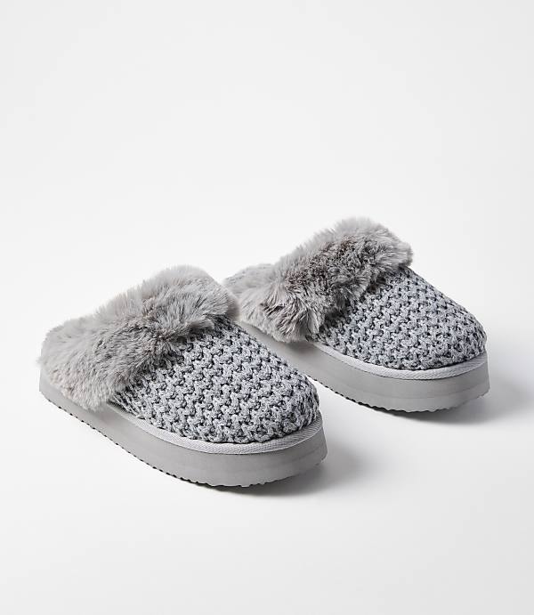 A pair of gray knitted slippers with faux fur trim rests on a white background.
