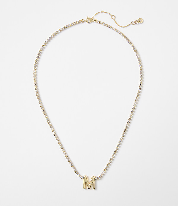 A gold necklace with a diamond-encrusted chain and a prominent "M" pendant rests on a plain white background.