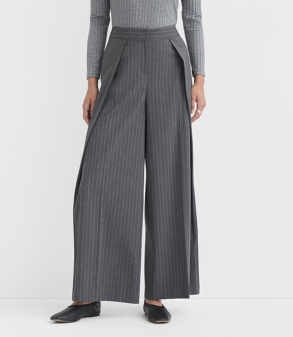 A person stands in wide-legged gray pinstripe pants and a gray long-sleeved shirt against a plain white background.