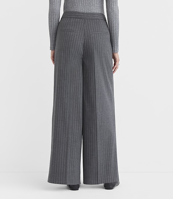 A person wearing gray pinstripe wide-leg pants and a gray sweater stands against a plain gray background.