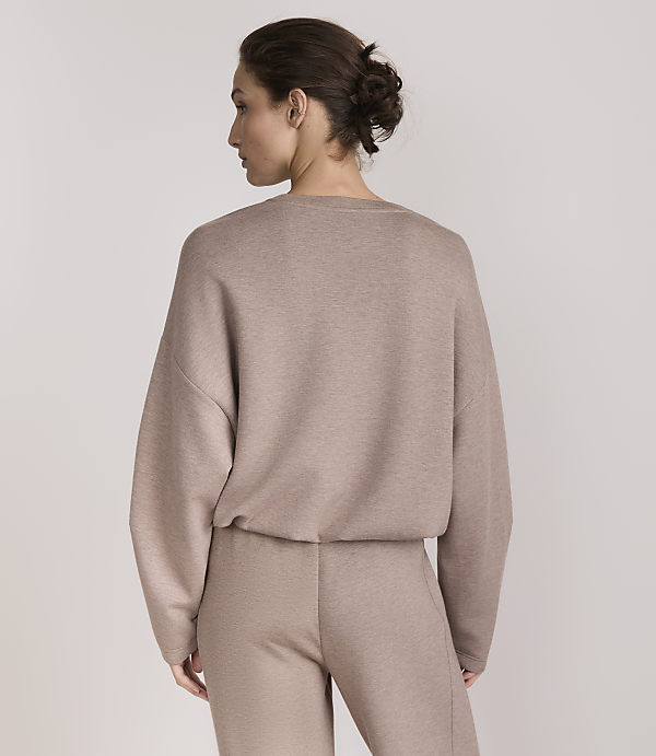 A woman in a taupe loungewear set stands against a plain, light gray background.