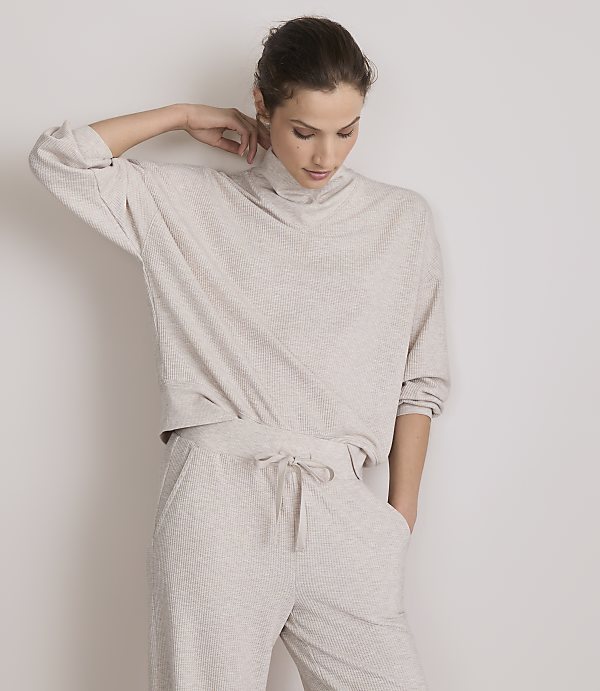 A woman in a beige loungewear set stands against a plain white background.