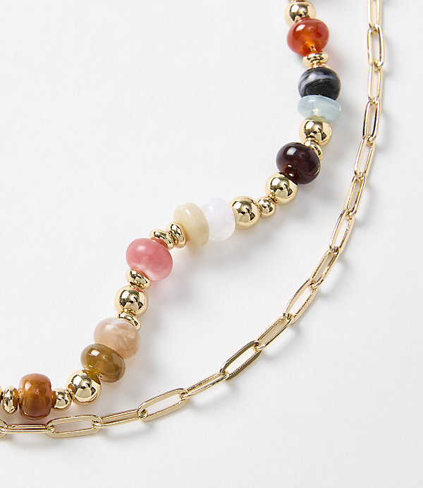 A close-up shot features a layered necklace with colorful beads and gold chain links against a plain white background.