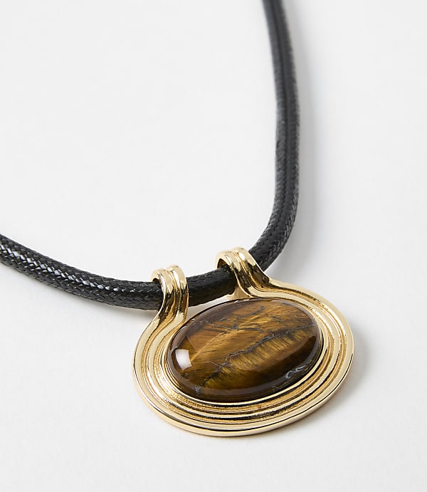 A gold pendant with a tiger's eye stone hangs from a black cord against a plain white background.