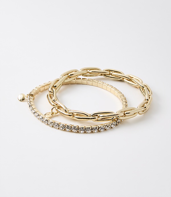 Two gold bracelets, one with a chunky chain design and the other with a band of small rhinestones, rest on a plain white background.