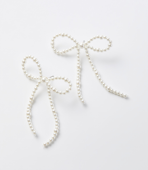 Two delicate pearl bow earrings with dangling strands are arranged on a plain white background.