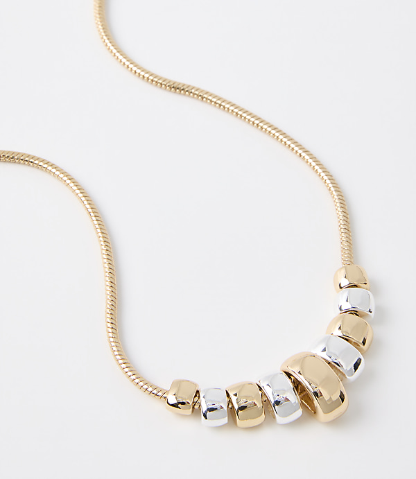 A gold snake chain necklace with alternating gold and silver beads is displayed against a plain white background.