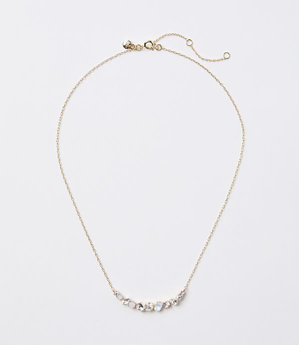 A delicate gold necklace with a curved arrangement of small, iridescent stones rests on a plain white background.