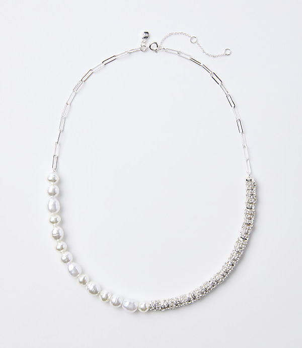 A delicate silver necklace with a chain of pearls on the left and a band of sparkling rhinestones on the right rests on a plain white background.
