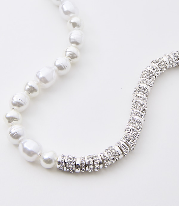 A pearl necklace with a section of sparkling silver beads curves across a white background.