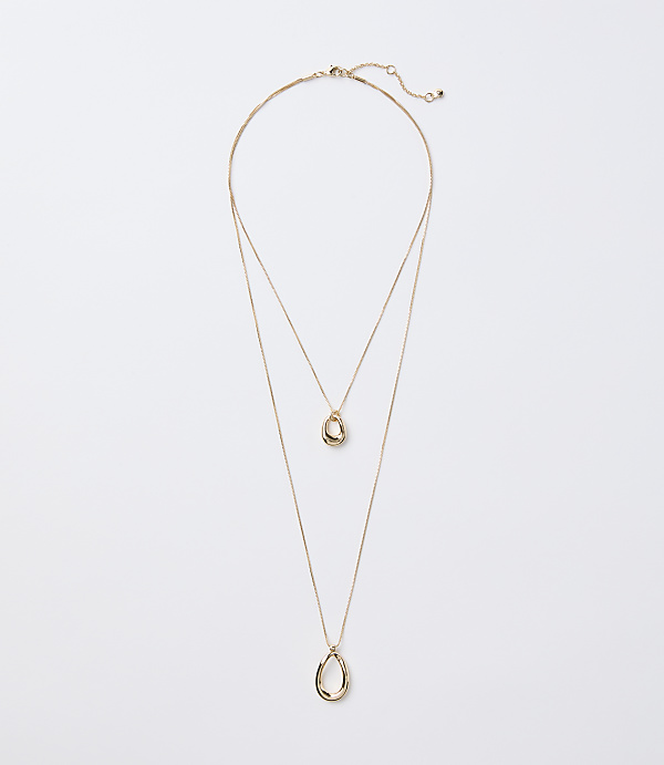 A delicate gold layered necklace with two abstract pendant shapes hangs against a plain white background.