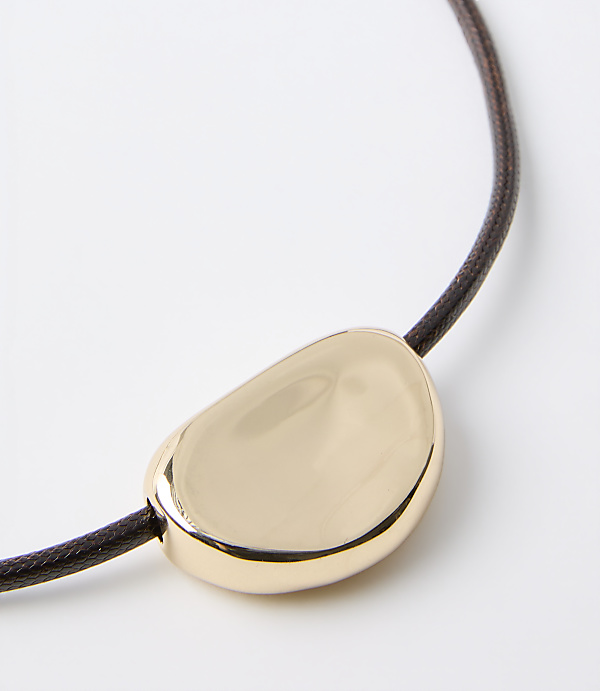 A smooth, golden pendant rests on a dark brown cord against a plain white background.