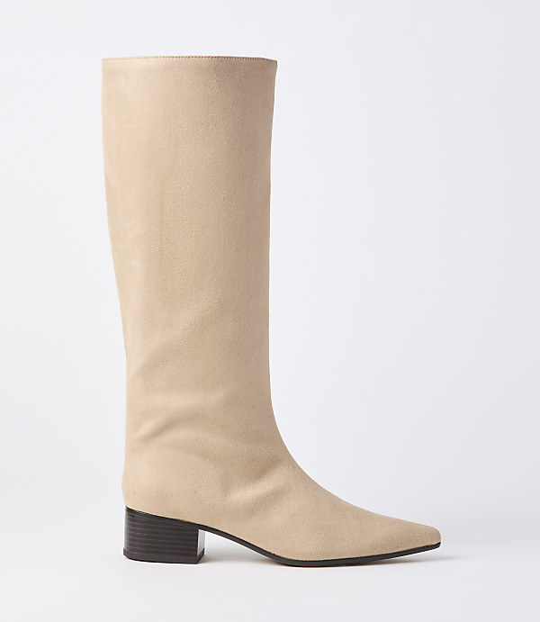 A beige suede knee-high boot with a pointed toe and a dark block heel stands against a plain white background.
