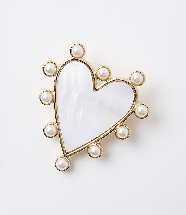 A white, heart-shaped brooch with a mother-of-pearl inlay and a border of small pearls sits against a plain white background.