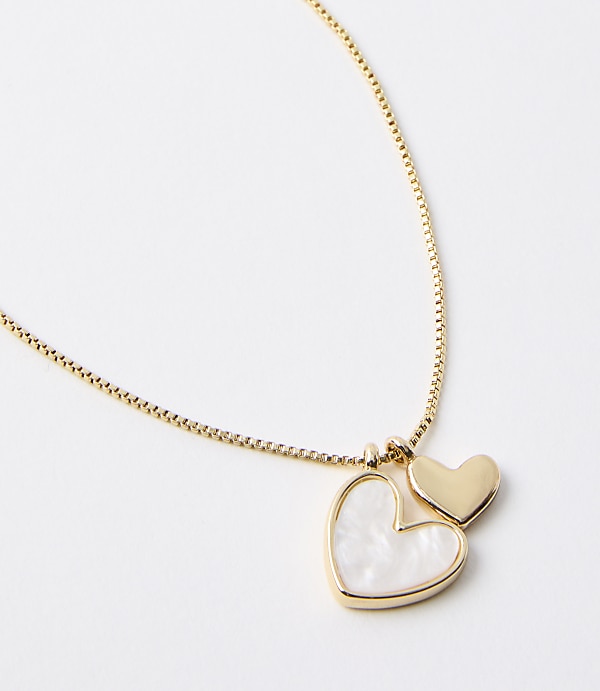 A delicate gold chain holds two heart-shaped pendants, one larger and inlaid with mother-of-pearl, against a plain white background.