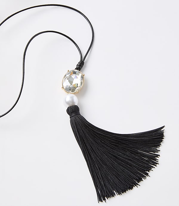 A black tassel necklace with a clear gem and pearl hangs against a plain white background.